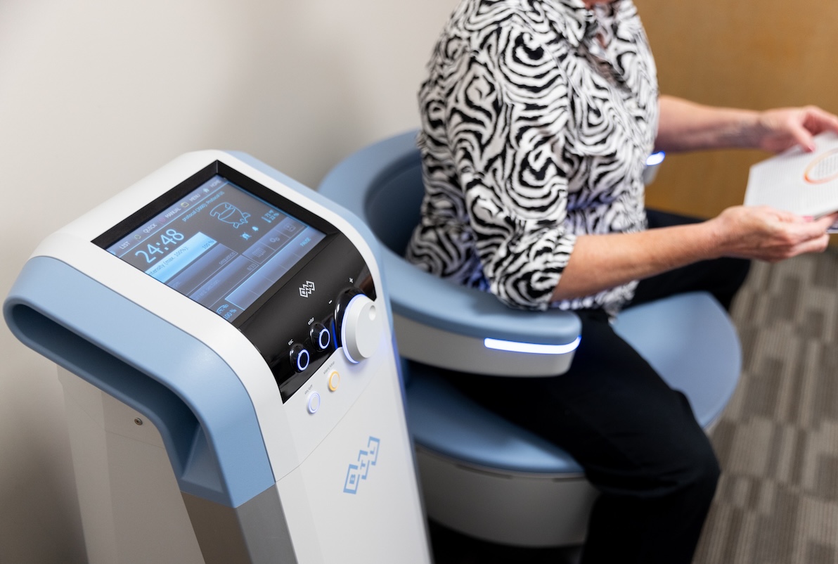 A woman sits on the Emsella chair and reads a magazine as she receives pelvic floor therapy.